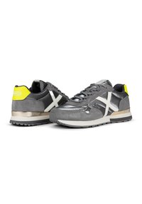Gray sneakers featuring a mix of suede and synthetic materials, a white cross design, a yellow accent on the heel, and a metallic midsole.