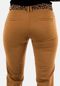 Bordeauxkleurige stretchy broek met een aangesloten silhouet, voorzien van een geblokte bordeaux- en beige tailleband en twee achterzakken. Soepele textuur.