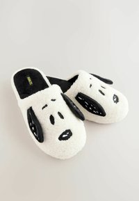 Bílé nadýchané pantofle s designem psí hlavy, mají černé akcenty na uších, nose a tlamě. Vyrobeno z měkké, texturované látky.