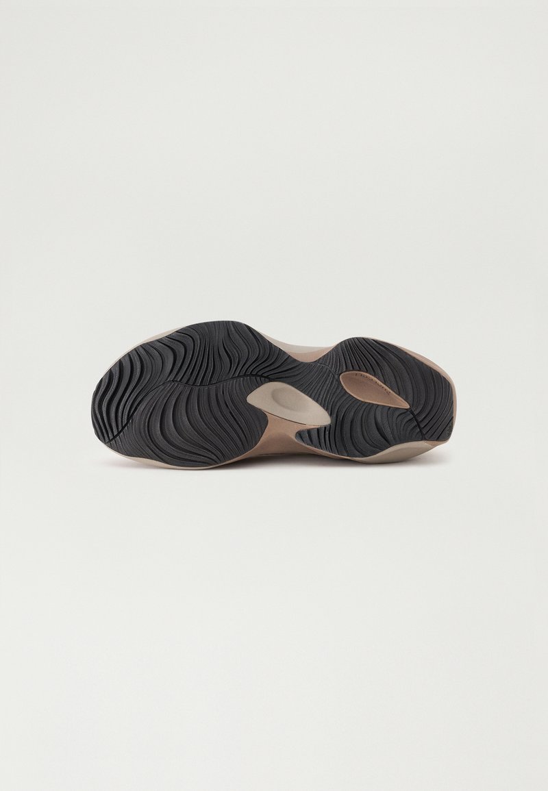 Suola della scarpa con una superficie in gomma nera testurizzata con motivi a onda, accentuata da aree lisce beige e ritagli per la flessibilità.