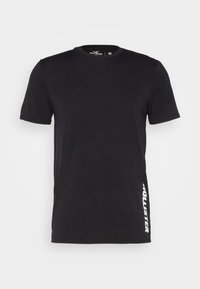 Černé bavlněné tričko s krátkým rukávem, kulatým výstřihem a bílým nápisem "HOLLISTER" tištěným vertikálně na levé straně. Měkká textura, standardní střih.