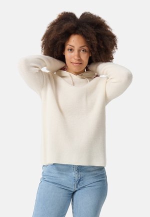 Light cream sweater with a ribbed texture and a hood, paired with light blue denim jeans. The sweater has long sleeves and a relaxed fit.