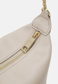 Beige leather handbag featuring a gold zipper closure, accentuated by a chain strap and textured surface. Compact and streamlined design.