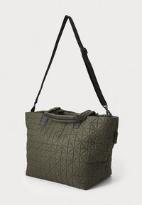 Laget olivengrønn totebag med svarte detaljer, med doble håndtak, justerbar stropp og geometrisk mønster på utsiden.