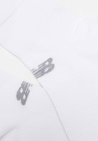 White crew socks made of textured fabric with a gray logo detail. The design features ribbed cuffs and a smooth finish throughout.