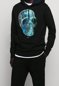 Černá mikina s kapucí s grafikou lebky v modrém odstínu na přední straně. Vyrobena z měkké látky, s kapucí na stažení a žebrovanými manžetami.