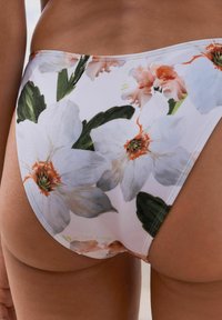 Due bikini floreale con sfondo bianco, grandi fiori bianchi e rosa, foglie verdi e una texture di tessuto liscia e elastica.
