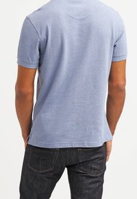 Polo en coton bleu à manches courtes, col côtelé, tissu légèrement texturé et ourlet droit. Porte avec un jean sombre.