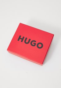 Rødt rektangulært eske med en glatt tekstur, med det svarte ordet "HUGO" tydelig plassert på den øverste flaten.