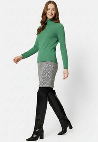 Grüner, gerippter Rollkragenpullover, eng anliegender Bleistiftrock mit schwarz-weißem Muster und schwarze kniehohe Stiefel mit Blockabsatz.