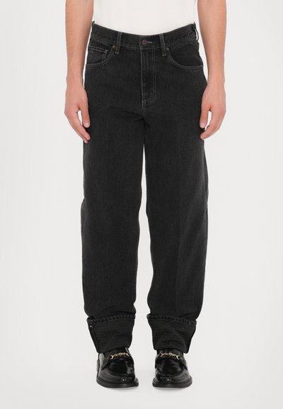 Jeans en denim noir avec une coupe droite, cinq poches et une fermeture à bouton. Le tissu a une texture subtile avec un léger dégradé. Manches retroussées.