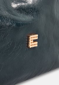 Gestructureerde donkerteal leren tas met een metallic gouden "E" accent, voorzien van een gladde afwerking en subtiele glans.