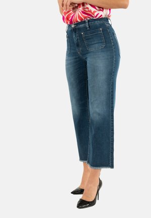 Jeans de mezclilla azul de pierna ancha con cintura alta, que presentan bolsillos delanteros y traseros, y dobladillo sin acabar. Combinados con zapatos de tacón alto negros.