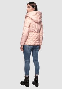Chaqueta de plumas acolchada rosa claro con capucha, cintura ceñida y mangas largas, combinada con jeans ajustados azules y botas de plataforma negras.