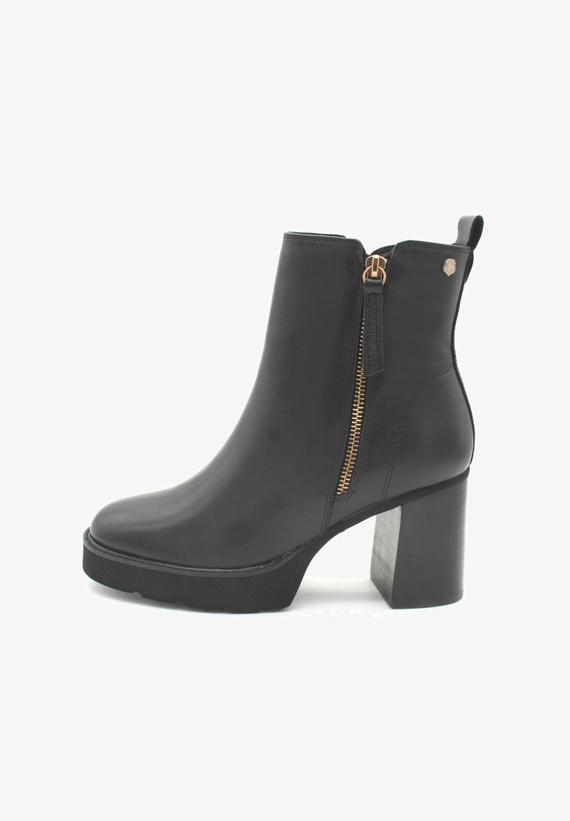 Botín negro de cuero hasta el tobillo con tacón grueso, cremallera lateral con tirador de cuero y un pequeño logo metálico cerca del borde superior.