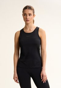 Camiseta deportiva sin mangas negra hecha de tela suave y elástica. Presenta un escote redondo y un logo centrado en el pecho.