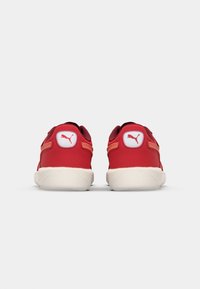 Baskets rouges avec une tige en tissu lisse et une semelle en caoutchouc blanche contrastante. Elles présentent un patch logo au niveau du talon et des accents sur les côtés dans une teinte plus claire.