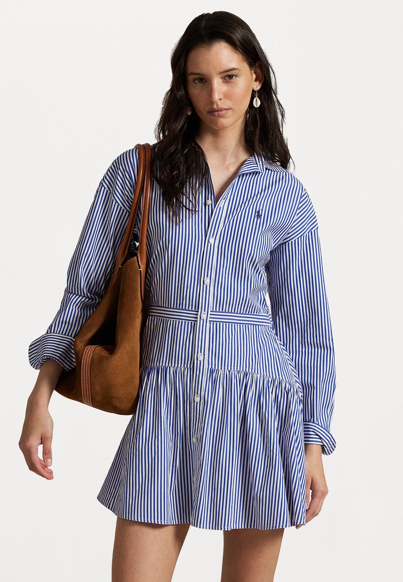 Striped blue and white shirt dress with long sleeves, button-down front, and gathered skirt. Paired with a brown suede shoulder bag.