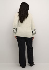 Ljusgrå tröja med svart blommigt broderi på ärmarna, kombinerad med svarta byxor, sedd från baksidan. Mjuk struktur, avslappnad passform.