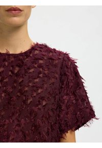 Bordeaux geklede top met een doorschijnende overlay, voorzien van rafelige accenten, een ronde halslijn, korte mouwen en een ongelijkmatige zoom.