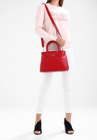 Sac à main en cuir rouge avec un design structuré, deux anses et une bandoulière amovible. Comprend des accessoires en argent et une finition brillante.
