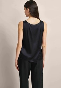Schwarzes Satin-Sleeveless-Top mit rundem Ausschnitt und glatter Textur, von hinten gezeigt, kombiniert mit locker sitzenden schwarzen Hosen.