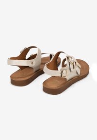 Helle beigefarbene Sandalen mit zwei verstellbaren Riemen und goldfarbigen Schnallen. Gepolsterte braune Innensohle mit strukturiertem Außensohle. Flaches Profildesign.