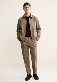 Giacca beige con colletto, camicia nera, pantaloni beige e scarpe nere. Taglio slim fit, trama liscia, design minimalista; senza motivi.