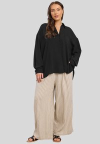 Blusa nera a maniche lunghe con scollatura a V e dettagli con bottoni, abbinata a pantaloni beige a righe ampie e sandali neri. Tessuto liscio.