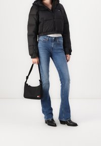 Czarna krótka kurtka puchowa, niebieskie dzwony oraz czarna torebka. Modelka nosi czarne botki na obcasie; dodatki obejmują torebkę na zamek.