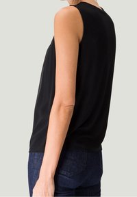 Schwarzes, ärmelloses Oberteil mit rundem Halsauschnitt, aus glattem Stoff und entspannter Passform, kombiniert mit dunkelblauer Jeans. Einfaches, vielseitiges Design.