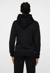 Svart hoodie i bomullsblandning. Har ribbade ärmslut och nederkant, slät yta och en kenguruficka framtill.