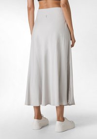 Jupe maxi gris clair au design fluide, dotée d'une fente sur le côté et d'une texture lisse. Associée à des baskets blanches.