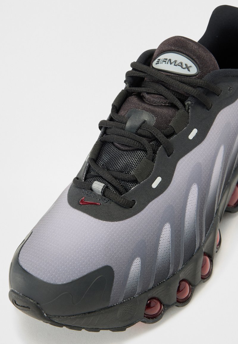 Der Nike Air Max Sneaker verfügt über ein graues Mesh-Obermaterial mit schwarzen Akzenten, eine Gummisohle, sichtbare Luftpolsterung und markante wellenförmige Designlinien.
