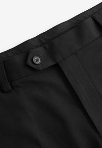 Schwarze Hose aus strukturiertem Stoff mit einem taillierten Taillenbund, einem einzelnen schwarzen Knopf und einer sauberen, scharfen Bügelfalte.