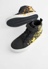 Schwarze High-Top-Sneaker mit buntem gelbem Spritzer-Muster, Schnürung vorne und weißer Gummisohle. Verfügt über einen Klettverschluss für einen sicheren Sitz.