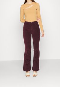 Long-sleeve, cutout mustard top paired with high-waisted, burgundy corduroy flared pants, finished with beige heeled sandals.