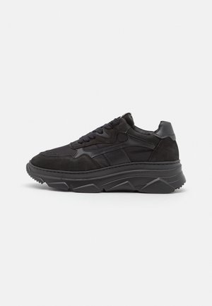 Czarny zamszowo-skórzany sneaker z grubą, teksturowaną podeszwą, wiązany z przodu, z wyściełanym kołnierzem, pokazany na białym tle z profilu.