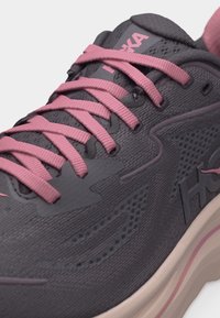 Κοντινό πλάνο σκούρου γκρι αθλητικού παπουτσιού με ροζ κορδόνια, ανώτερο μέρος από διαπνέον δίχτυ και λευκή σόλα με ροζ λεπτομέρειες.