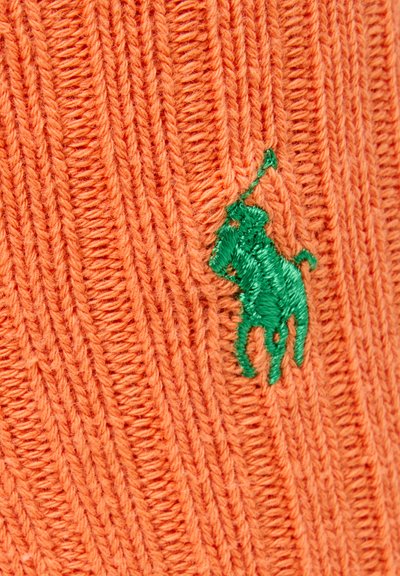 Oranje gebreide stof met een geribbelde textuur en een groene geborduurde polospelerlogo. Close-upweergave benadrukt de stikdetails.