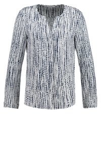 Blouse à manches longues pour femme avec base blanche et motif irrégulier de points bleus marins verticaux, dotée d'un col rond avec une petite découpe en V.