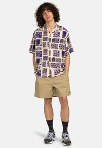 Short-sleeve shirt with a purple and cream square pattern, paired with beige shorts. Worn with black socks and patterned sneakers.