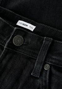 Jeans de mezclilla negra con una etiqueta que dice "Two Soon", tamaño 31/32, y un botón de metal grabado con el nombre de la marca.
