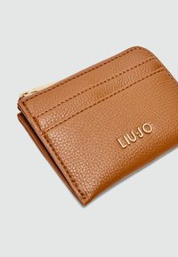 Brown leather wallet with a textured surface, featuring card slots and a zip pocket. Embossed logo in gold on the front.