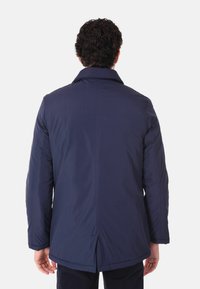Giacca imbottita blu navy con colletto, slim fit e taglio dritto; presenta uno spacco posteriore evidente e una texture liscia e opaca.