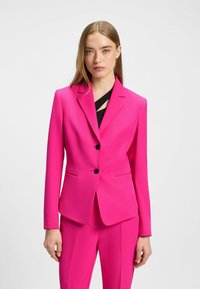 Blazer fuchsia à deux boutons, avec des revers crantés et des poches à rabat à l'avant. Présente une texture lisse et une coupe structurée, associé à un pantalon assorti.