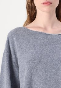 Suéter cinza de malha com um decote amplo, textura suave e detalhe canelado nas bordas, com um ajuste ligeiramente solto.