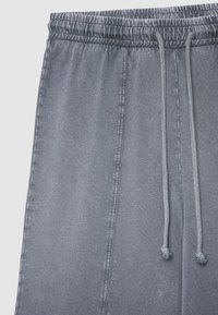 Graue Jogginghosen mit elastischem Bund, Kordelzugverschluss, weicher Textur und dezentem Glanz. Verfügt über Seitennaht und eine lockere Passform.