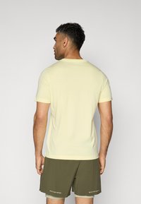 Light yellow short-sleeve t-shirt with a round neckline, smooth texture, worn with olive green shorts featuring white text accents.