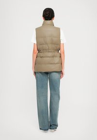 Beige gewatteerd vest met hoge kraag en nauwsluitende taille, gecombineerd met lichtblauwe wijdse jeans. Soepele textuur en minimalistisch ontwerp.